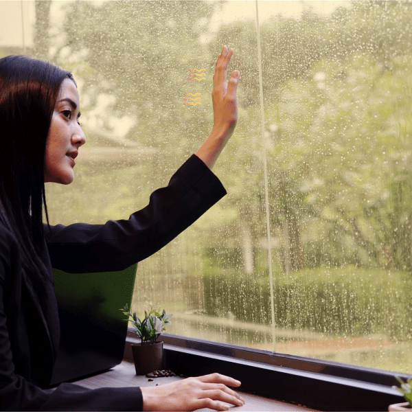 woman looking out of rain soaked glass window